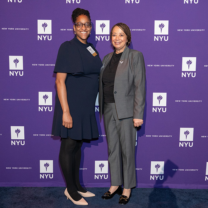 Melissa Ojemeni and another woman standing in front of NYUAA Awards banner