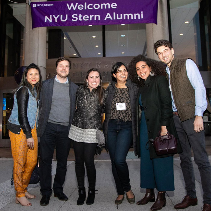 Group of men and women in gathered in front of welcome NYU Stern alumni banner